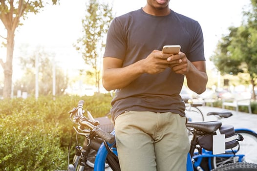 a black man leaning against a parked bike looking at his phone